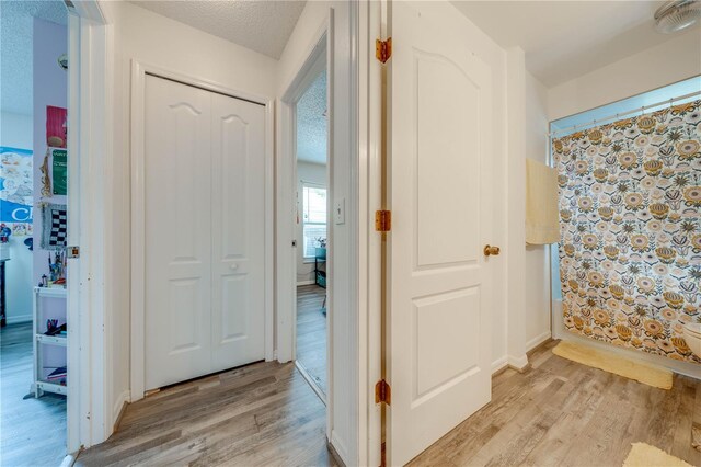 hall featuring light wood-type flooring and a textured ceiling