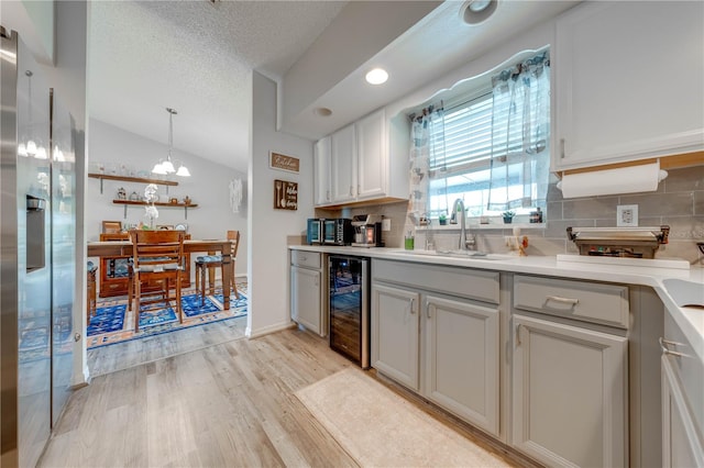 kitchen with wine cooler, backsplash, light hardwood / wood-style floors, vaulted ceiling, and sink