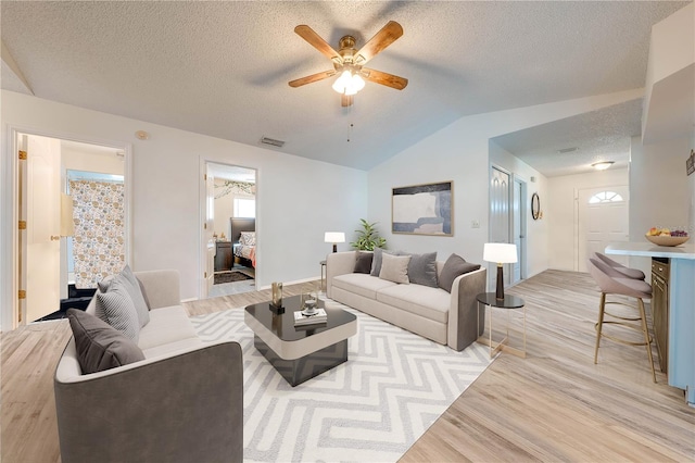 living room featuring lofted ceiling, light hardwood / wood-style floors, a textured ceiling, and ceiling fan