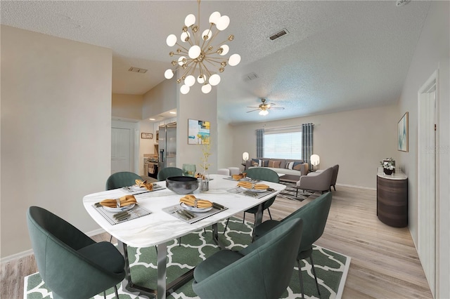 dining area with vaulted ceiling, ceiling fan with notable chandelier, a textured ceiling, and light wood-type flooring