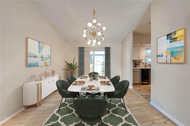 dining space with light hardwood / wood-style floors, beverage cooler, vaulted ceiling, and a chandelier