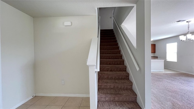 stairway with a chandelier, tile patterned flooring, and a textured ceiling