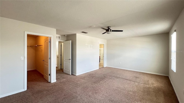 unfurnished bedroom with carpet flooring, a textured ceiling, ceiling fan, a closet, and a walk in closet