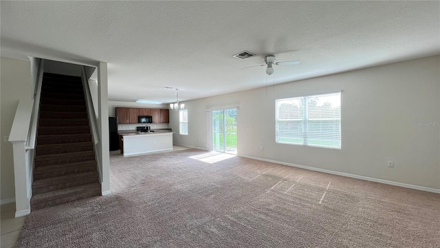 unfurnished living room featuring ceiling fan with notable chandelier, a textured ceiling, and light carpet