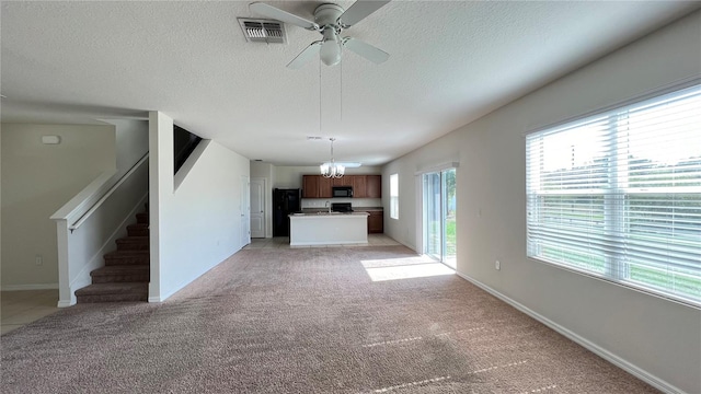 unfurnished living room with a textured ceiling, light carpet, and ceiling fan with notable chandelier