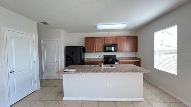 kitchen with black appliances, a textured ceiling, light tile patterned floors, sink, and a kitchen island with sink