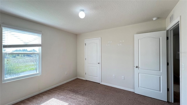 unfurnished bedroom with a textured ceiling and dark carpet