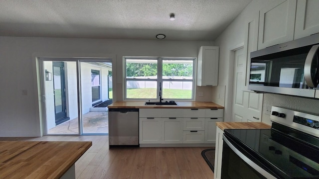 kitchen with stainless steel appliances, white cabinetry, wooden counters, and light wood-type flooring