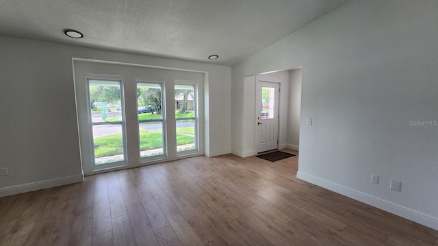 doorway to outside featuring a textured ceiling, plenty of natural light, vaulted ceiling, and light wood-type flooring