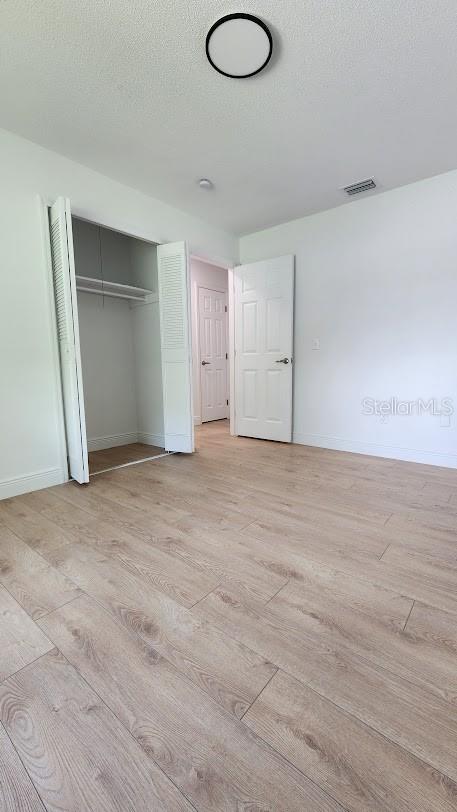 unfurnished bedroom with a closet, light hardwood / wood-style flooring, and a textured ceiling