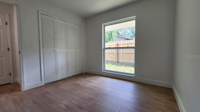 unfurnished bedroom with a closet, light hardwood / wood-style flooring, and multiple windows