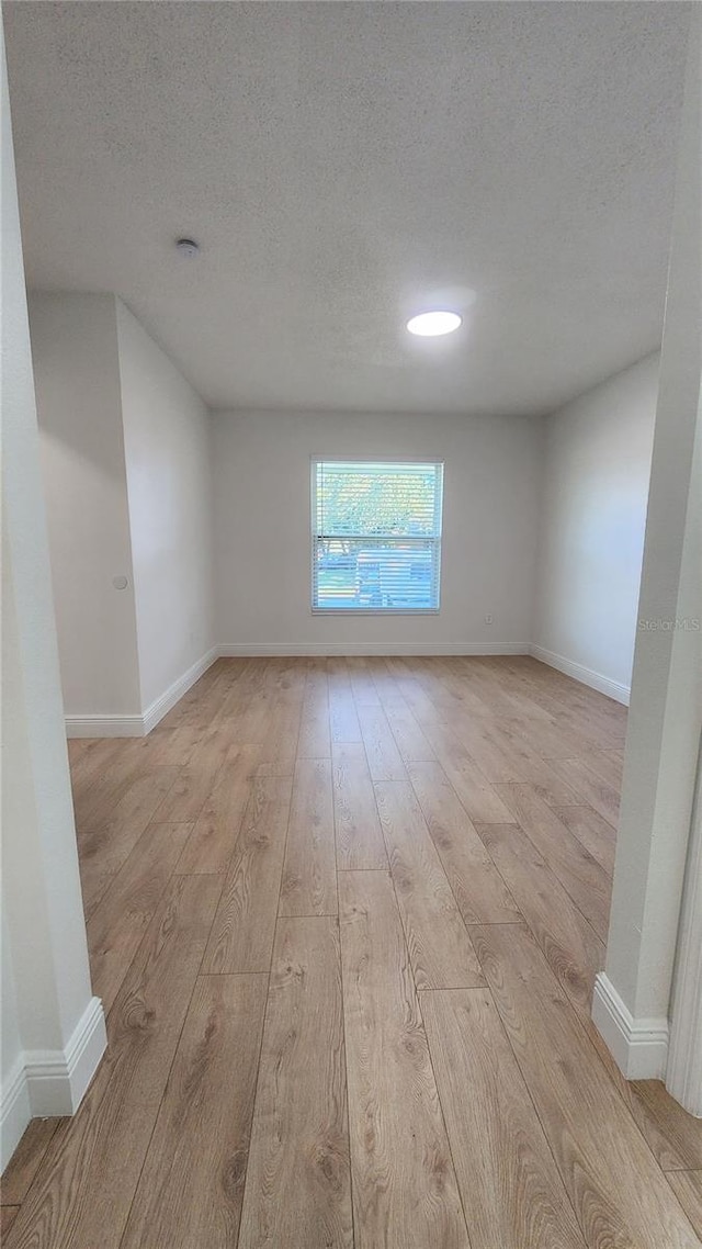 unfurnished room with light wood-type flooring and a textured ceiling