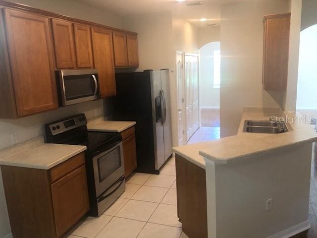 kitchen featuring light tile patterned flooring, appliances with stainless steel finishes, kitchen peninsula, and sink