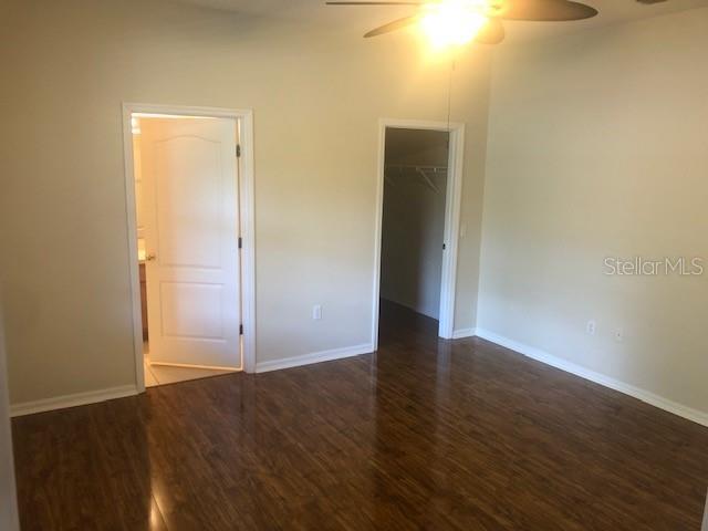 unfurnished bedroom featuring connected bathroom, a walk in closet, dark hardwood / wood-style floors, a closet, and ceiling fan