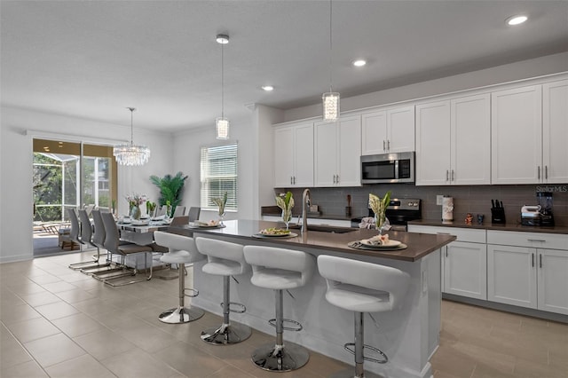 kitchen featuring decorative light fixtures, an island with sink, sink, white cabinets, and stainless steel appliances