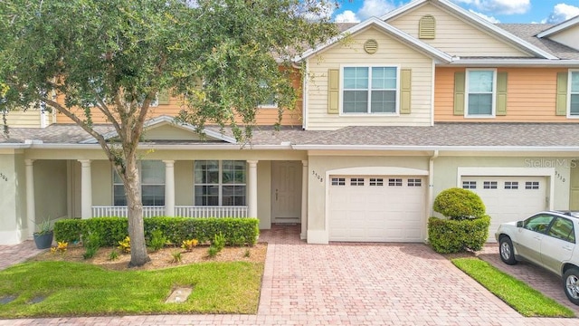 townhome / multi-family property with a garage, driveway, a shingled roof, and stucco siding