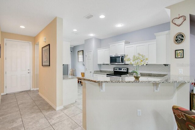 kitchen with appliances with stainless steel finishes, kitchen peninsula, white cabinets, and light stone countertops