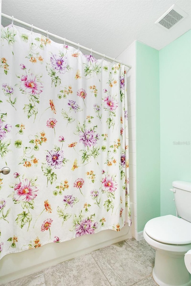 bathroom with tile patterned flooring, toilet, shower / bath combination with curtain, and a textured ceiling