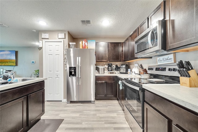 kitchen featuring a textured ceiling, dark brown cabinets, light hardwood / wood-style flooring, appliances with stainless steel finishes, and sink