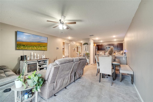 living room featuring ceiling fan, light colored carpet, and a textured ceiling