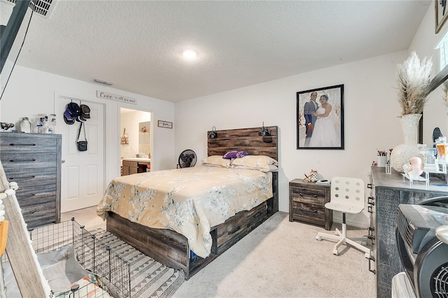 bedroom with a textured ceiling, light carpet, and ensuite bath