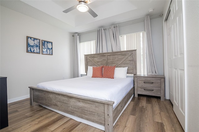 bedroom with a tray ceiling, a closet, hardwood / wood-style floors, and ceiling fan