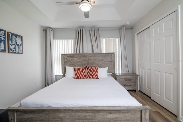 bedroom with hardwood / wood-style flooring, ceiling fan, a raised ceiling, and a closet