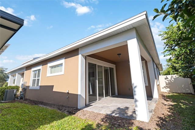 back of property with central AC unit, a patio, and a lawn