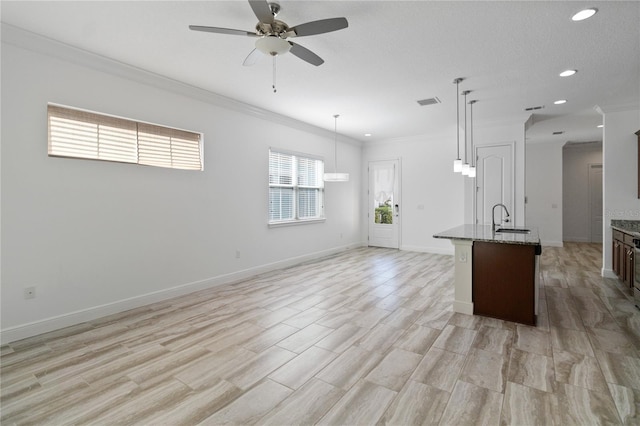 kitchen with pendant lighting, sink, crown molding, a kitchen island with sink, and dark stone countertops