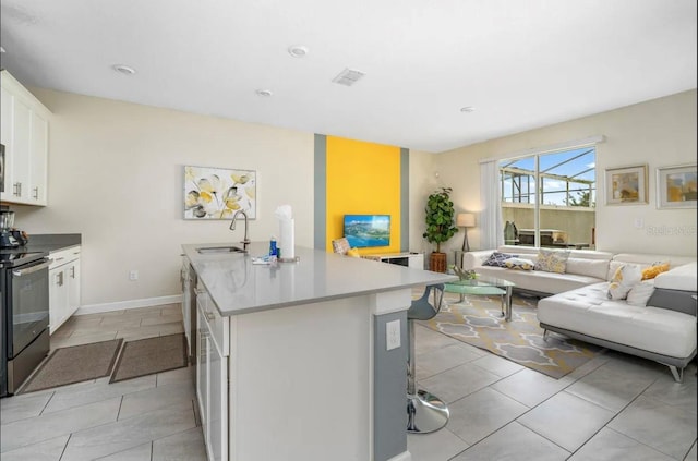 kitchen with sink, white cabinetry, electric stove, and an island with sink