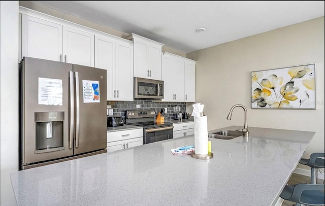 kitchen featuring white cabinetry, backsplash, a kitchen bar, stainless steel appliances, and sink