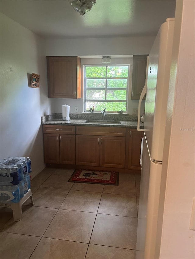 kitchen featuring sink, white fridge, dark stone countertops, and light tile patterned floors