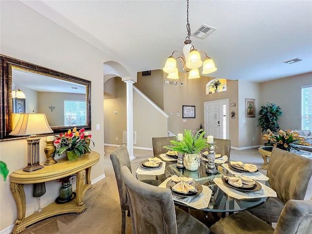 carpeted dining space featuring plenty of natural light, ornate columns, and an inviting chandelier