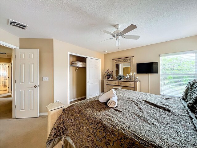 bedroom with ceiling fan, a closet, a textured ceiling, and light carpet