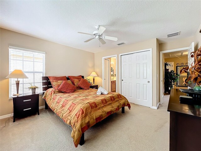 bedroom featuring ceiling fan, light colored carpet, ensuite bathroom, and a textured ceiling