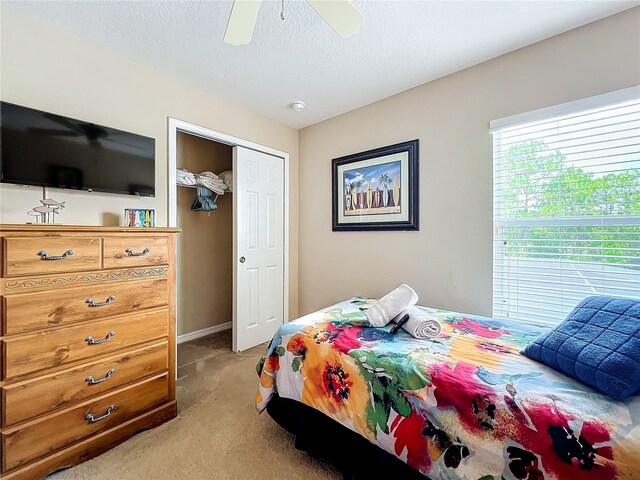 carpeted bedroom with ceiling fan, a closet, and a textured ceiling