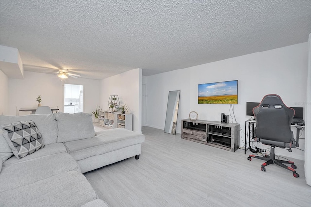 living room with ceiling fan, light wood-type flooring, and a textured ceiling