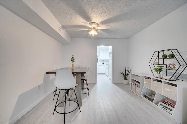 dining space featuring light wood-type flooring, ceiling fan, and a textured ceiling