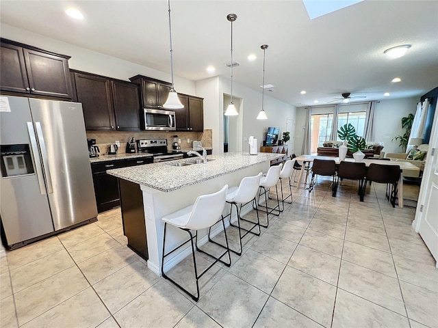 kitchen featuring decorative light fixtures, tasteful backsplash, ceiling fan, an island with sink, and appliances with stainless steel finishes