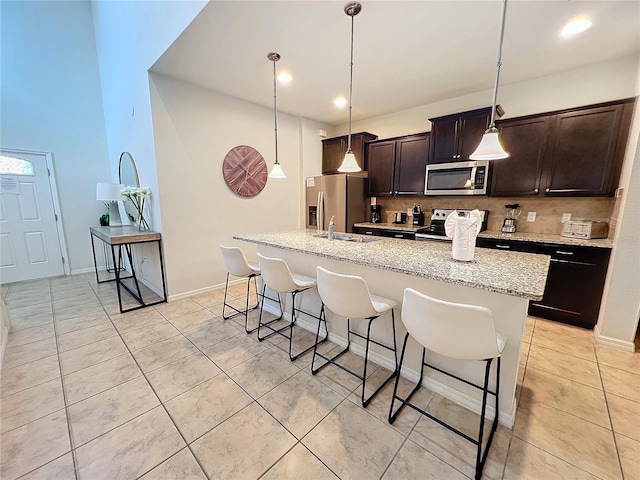 kitchen with appliances with stainless steel finishes, a kitchen island with sink, decorative backsplash, a kitchen bar, and decorative light fixtures