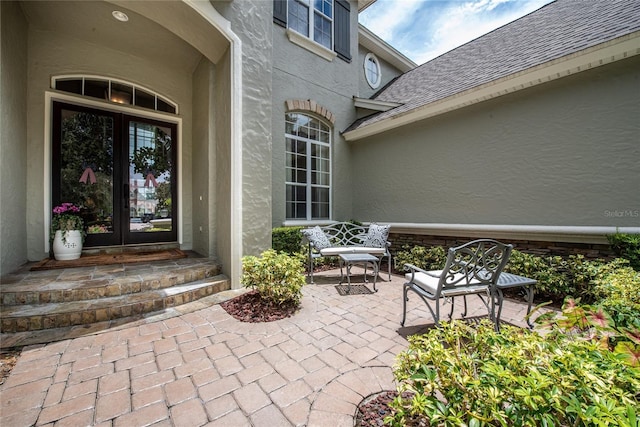 entrance to property featuring french doors, roof with shingles, and stucco siding