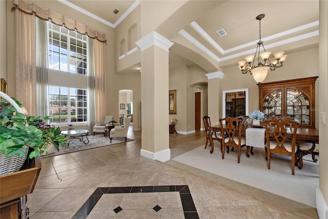 tiled dining room with an inviting chandelier, decorative columns, a high ceiling, crown molding, and a raised ceiling