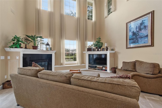 living room featuring light carpet, a high ceiling, and a glass covered fireplace