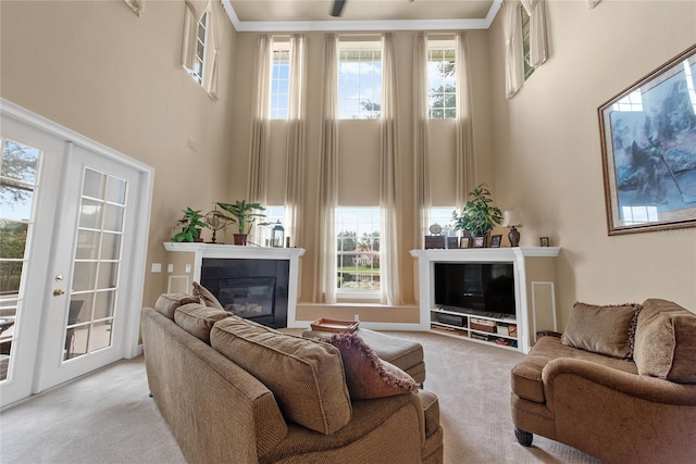 living room with light colored carpet, a towering ceiling, french doors, a tiled fireplace, and crown molding