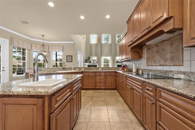 kitchen featuring crown molding, a center island with sink, brown cabinets, and a sink