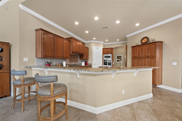 kitchen featuring appliances with stainless steel finishes, a breakfast bar, brown cabinets, light stone counters, and a peninsula