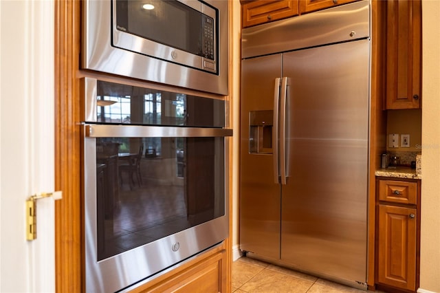 kitchen featuring built in appliances, light stone countertops, and light tile patterned floors