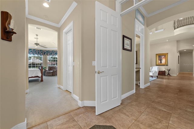 corridor featuring arched walkways, light tile patterned floors, light carpet, baseboards, and ornamental molding