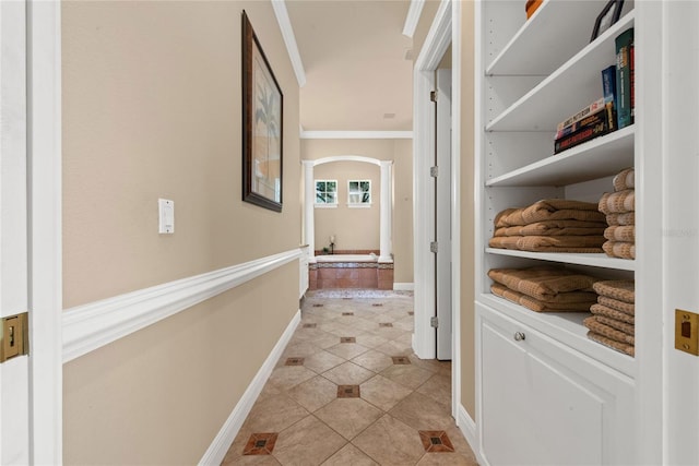 corridor featuring baseboards, arched walkways, crown molding, and light tile patterned flooring