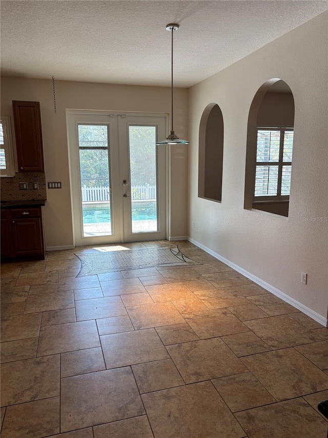 unfurnished dining area featuring french doors and a textured ceiling